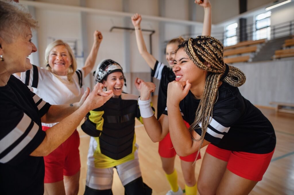 Group of young and old cheerful women, floorball team players, in gym cebrating victory.